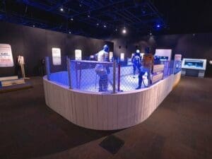 A fenced indoor exhibit at the St. Louis Science Center features mannequins in work uniforms and helmets, informational displays, and dim blue lighting—offering summer fun in a spacious room.
