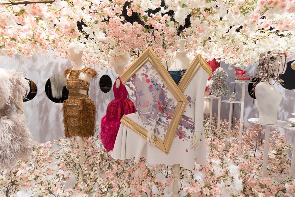 mannequins with dresses and flowers in a room with white walls and a white wall with pink flowers and a white wall with a white wall with pink flowers and a white wall with a gold