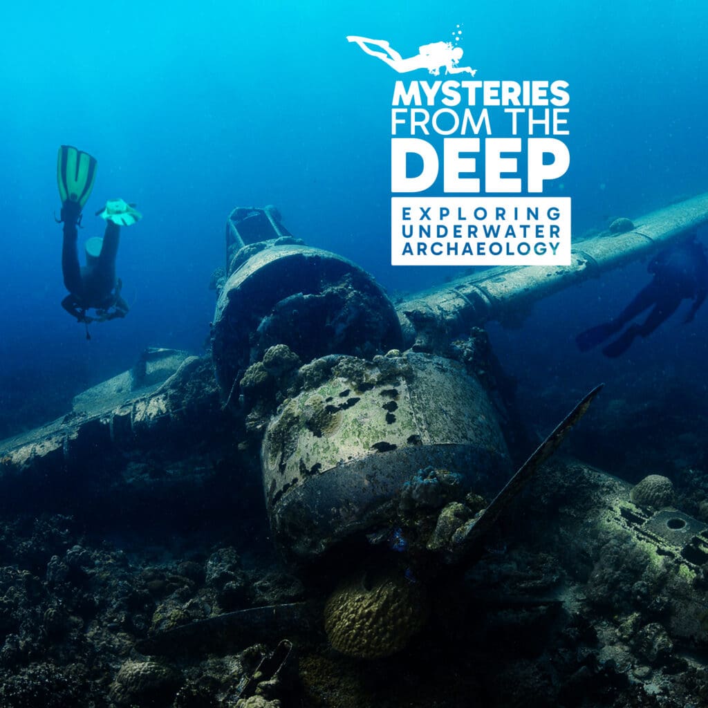 Two scuba divers explore a sunken, coral-covered airplane wreck underwater beneath the title "Mysteries from the Deep: Exploring Underwater Archaeology," part of a captivating touring exhibition.